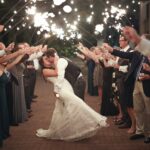 A bride and groom kissing while people hold up sparklers over them.